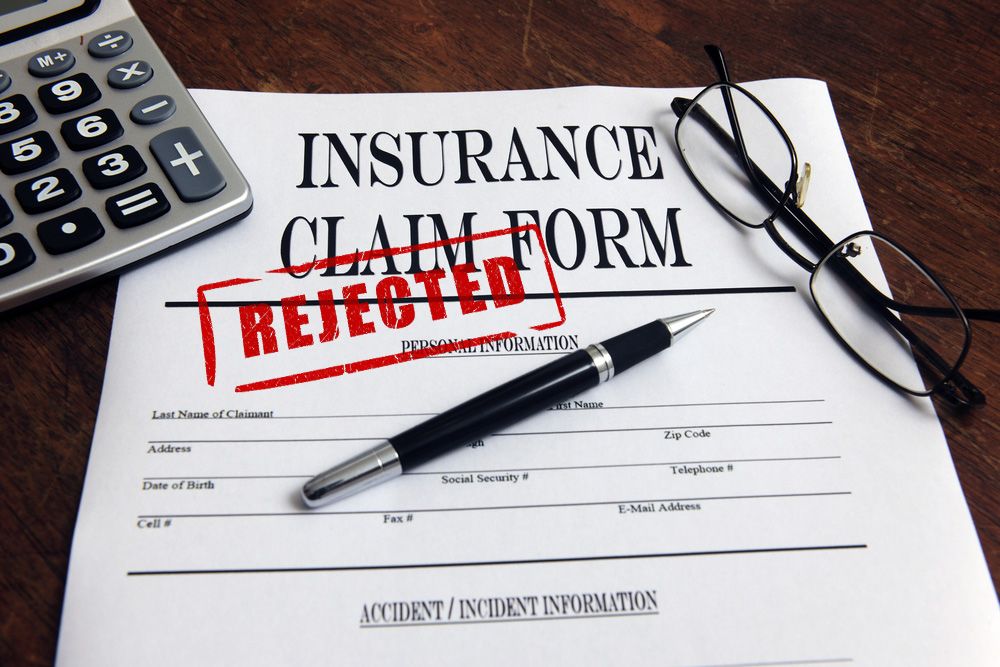 Rejected insurance claim form, pen, glasses and calculator